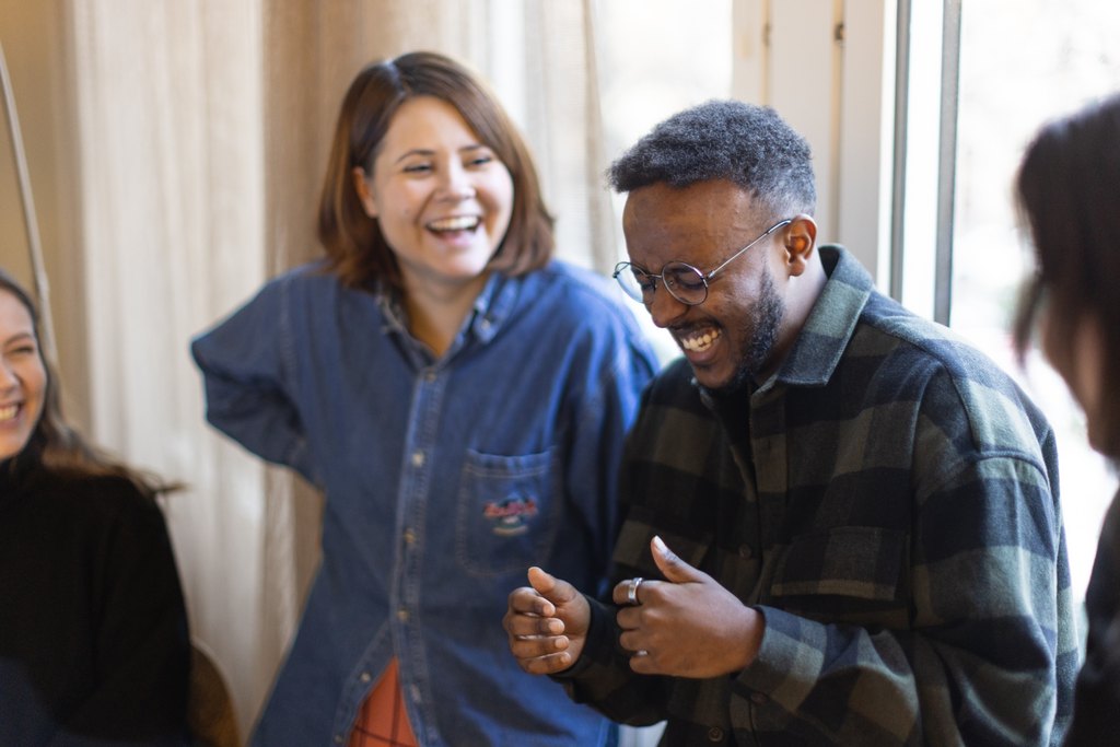 Two people sitting next to each other with laptops in their laps, both laughing.