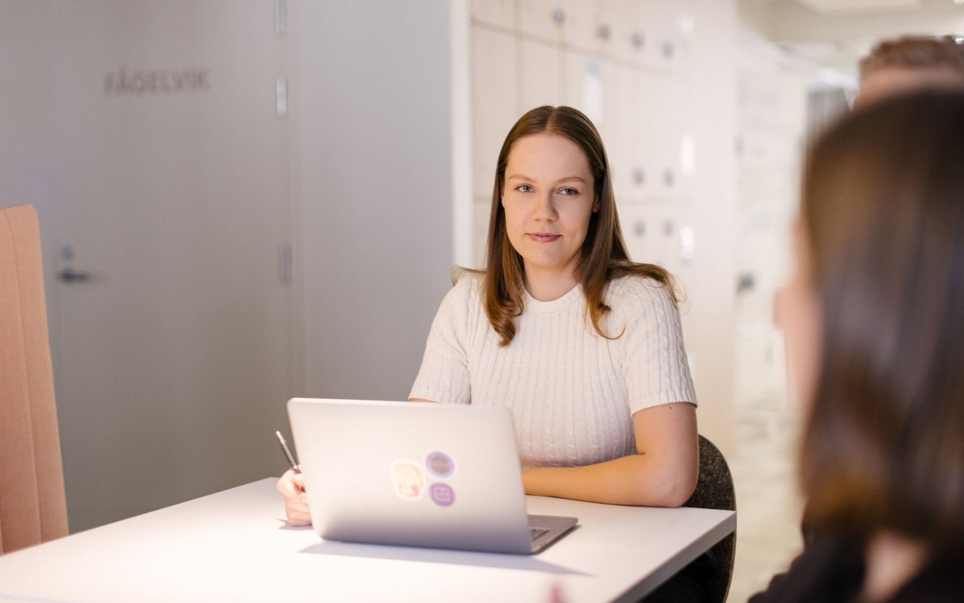Woman sitting in a table looking at another person with a laptop in front of her