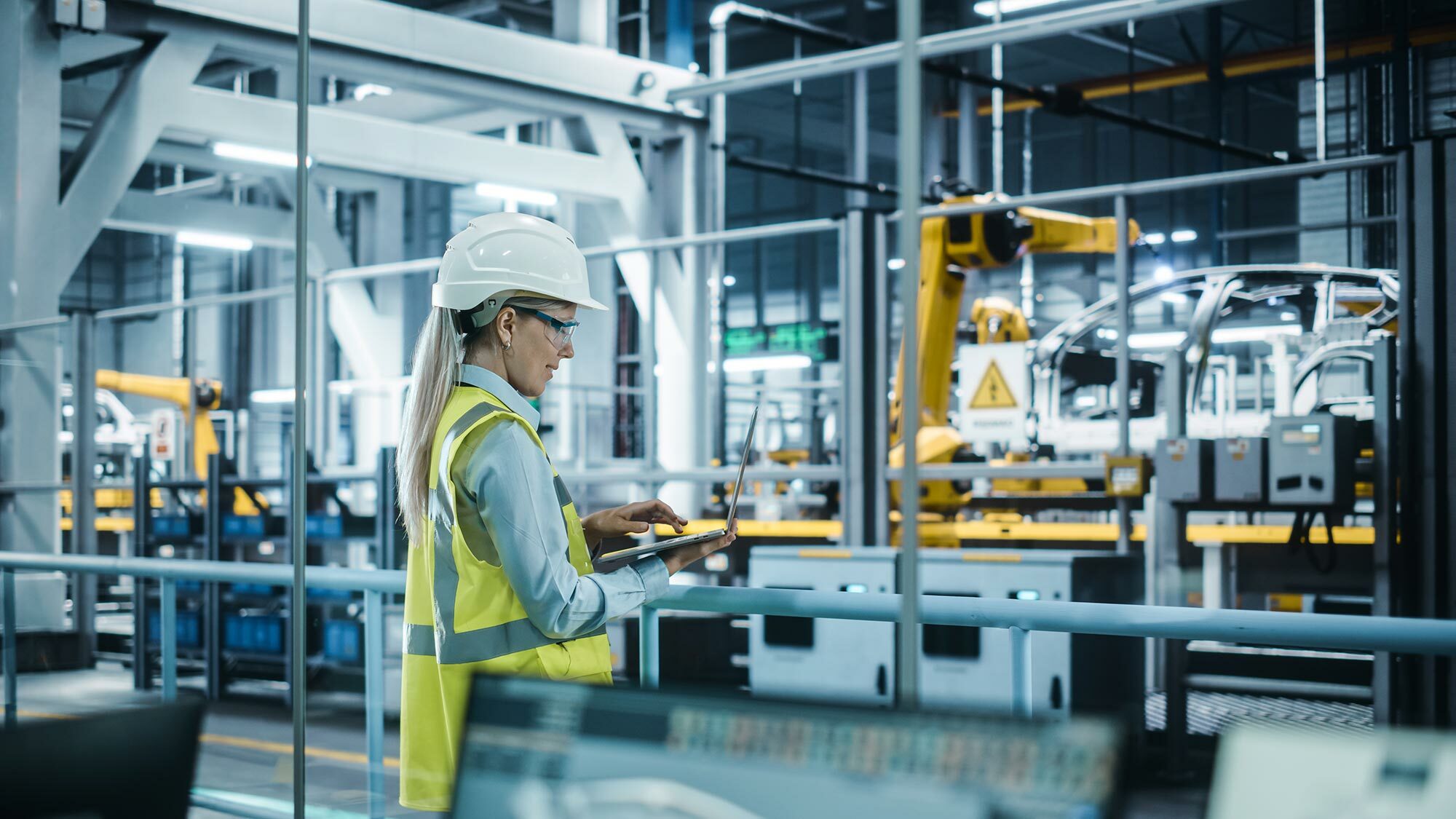 Woman with laptop standing in auto factory