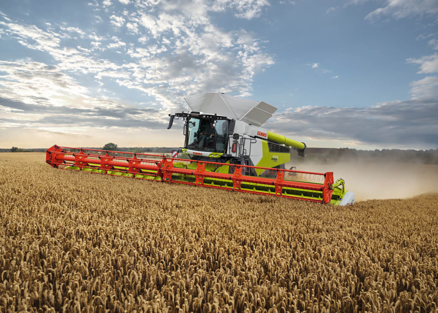 Suuri leikkuupuimuri työskentelee kypsällä viljapellolla kirkkaan taivaan alla, leikatessaan viljaa leveällä etuleikkurilla ja jättäen taakseen pölyvanan.