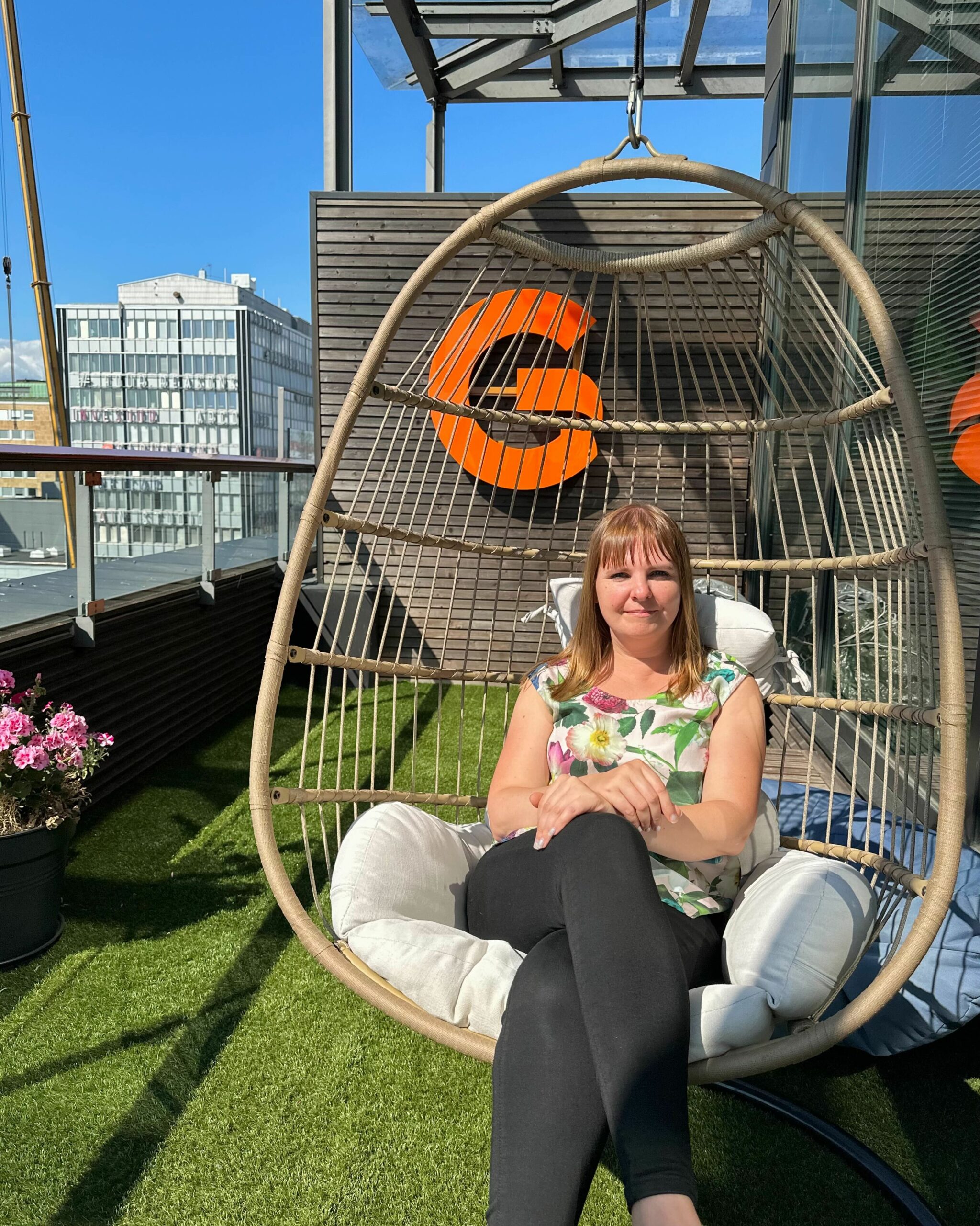 A person sitting on a swing, there is a big G-light and a cityscape in the background.