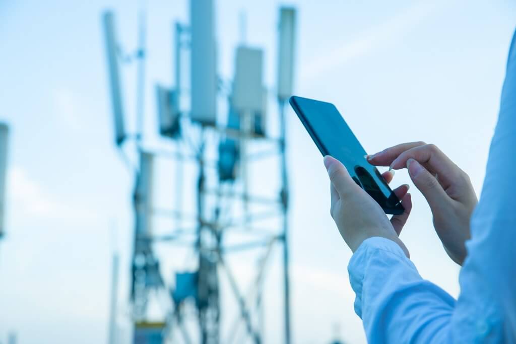 picture of a persons hands holding and using a mobile device in front of a link mast